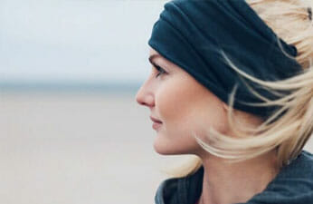 Profile of beautiful woman with blonde hair wearing a blue headband looking at the beach horizon.