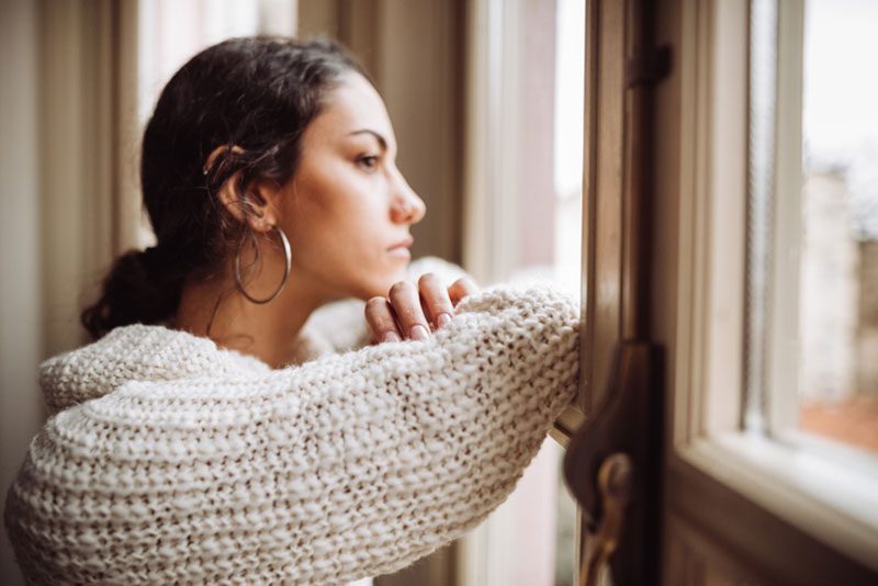 Young woman wearing earrings and a sweater looking out a window.