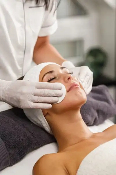 Woman receiving a facial with a dark pillow behind her hed and swabs on her cheeks
